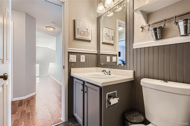 bathroom with hardwood / wood-style floors, vanity, lofted ceiling, toilet, and a textured ceiling