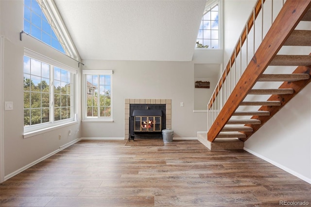 13873 E Lehigh Ave Unit B, Aurora, CO 80014 - unfurnished living room featuring plenty of natural light, high vaulted ceiling, wood finished floors, stairs, and a tile fireplace
