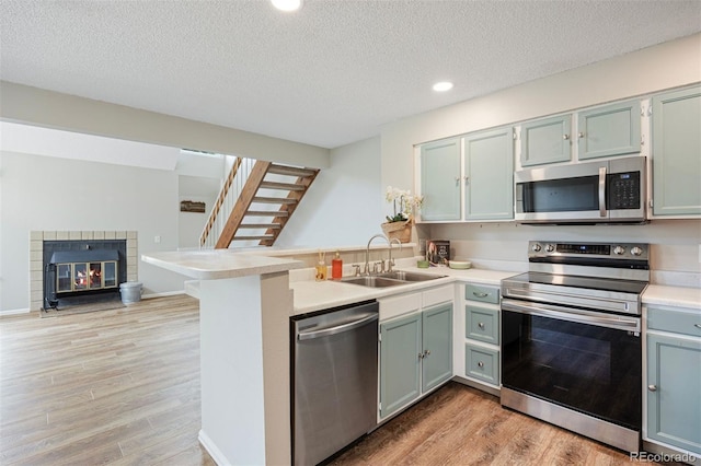 13873 E Lehigh Ave Unit B, Aurora, CO 80014 - kitchen featuring appliances with stainless steel finishes, a peninsula, a textured ceiling, light wood-style floors, and light countertops