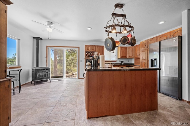 kitchen featuring hanging light fixtures, ceiling fan, light tile patterned floors, stainless steel fridge with ice dispenser, and a wood stove