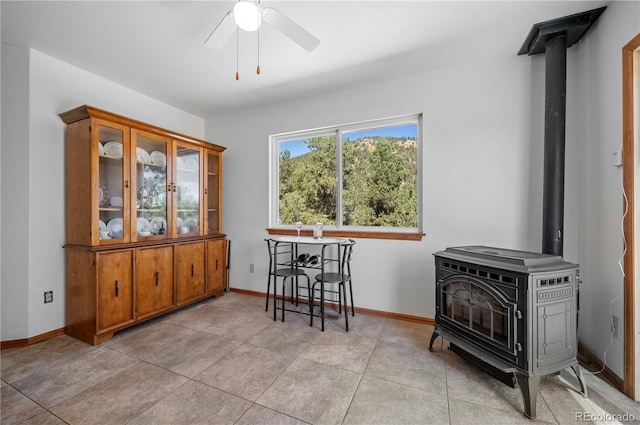 dining space featuring ceiling fan, a wood stove, and light tile patterned flooring