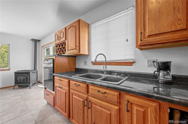 kitchen with sink, light tile patterned flooring, a wood stove, and plenty of natural light