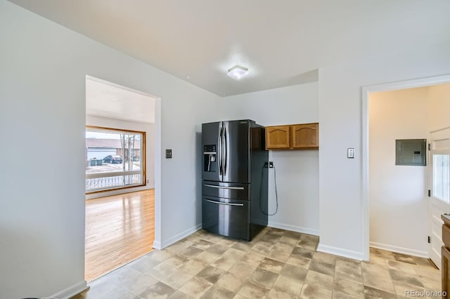 kitchen featuring electric panel, baseboards, brown cabinets, and fridge with ice dispenser