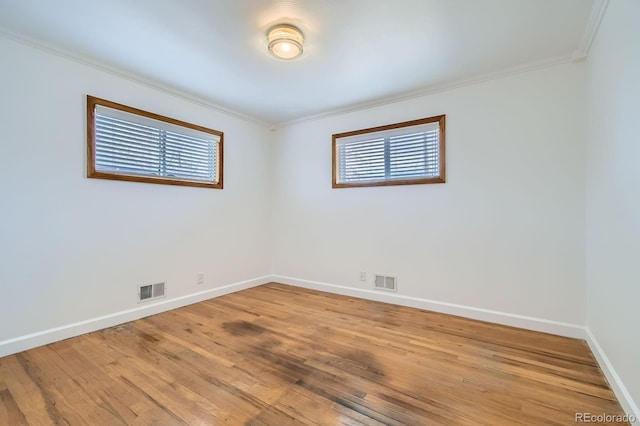 empty room featuring light wood-style flooring, crown molding, baseboards, and visible vents