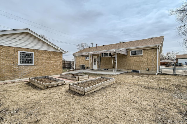 rear view of house with fence, a patio, brick siding, cooling unit, and a vegetable garden