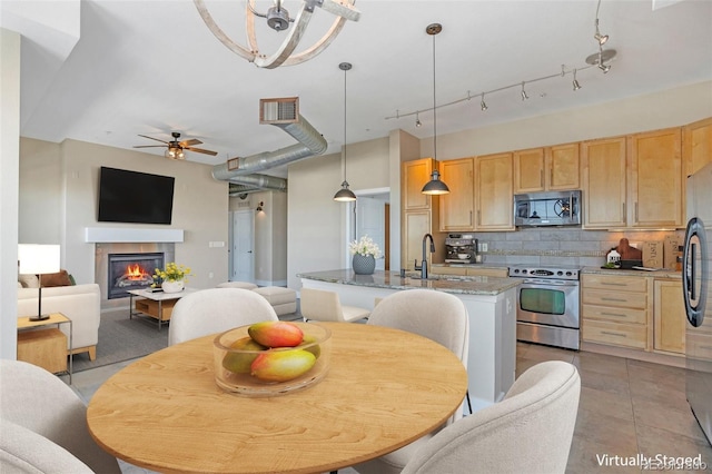 kitchen featuring pendant lighting, appliances with stainless steel finishes, light brown cabinets, dark stone countertops, and sink