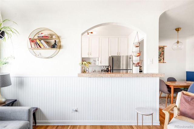 kitchen featuring light wood-type flooring, freestanding refrigerator, a peninsula, a breakfast bar area, and white cabinets