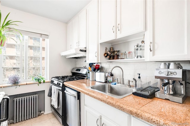 kitchen featuring under cabinet range hood, radiator heating unit, appliances with stainless steel finishes, white cabinets, and a sink