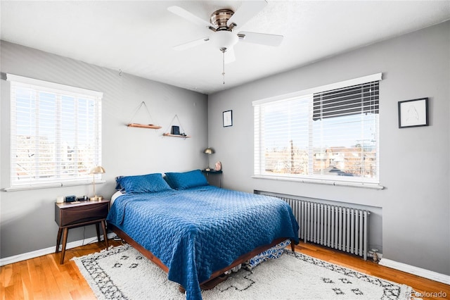 bedroom with multiple windows, radiator heating unit, baseboards, and wood finished floors