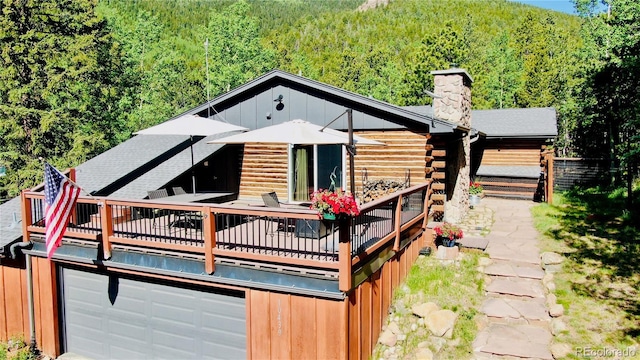 10439 Christopher Dr, Conifer, CO 80433 - rear view of house featuring a wooded view, log exterior, a chimney, a wooden deck, and a garage