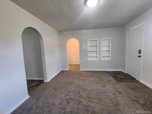 unfurnished room featuring built in features, dark carpet, and a textured ceiling