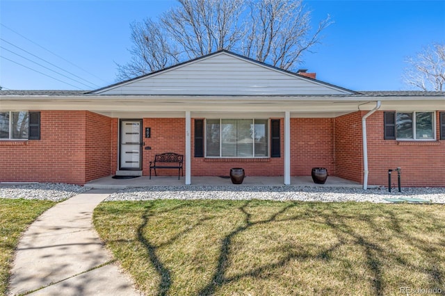 view of front of house with a front lawn, a porch, brick siding, and a chimney