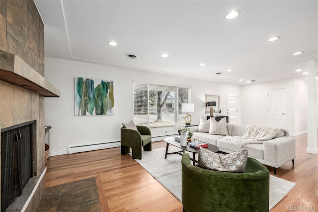 living area featuring a baseboard heating unit, visible vents, wood finished floors, and a fireplace