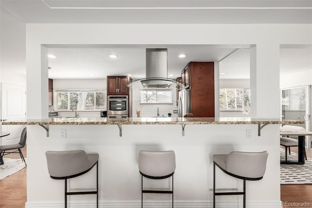 kitchen with island exhaust hood, stainless steel appliances, a kitchen breakfast bar, and wood finished floors