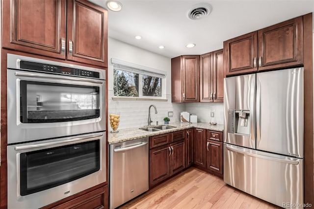 kitchen featuring light stone countertops, visible vents, a sink, decorative backsplash, and appliances with stainless steel finishes