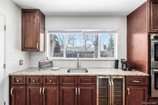 kitchen with beverage cooler, stainless steel double oven, tasteful backsplash, and a sink