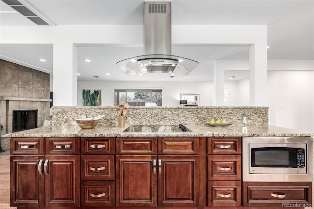 kitchen featuring stainless steel microwave, visible vents, light stone countertops, island exhaust hood, and black electric cooktop