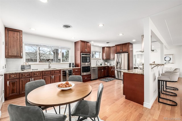 kitchen featuring wine cooler, decorative backsplash, appliances with stainless steel finishes, light wood-style floors, and a sink