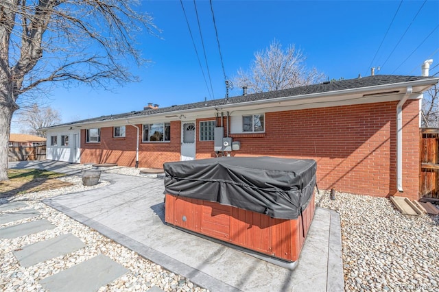 back of property featuring brick siding, a hot tub, a patio, and fence