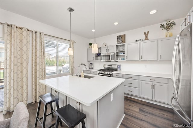 kitchen with a breakfast bar area, a sink, stainless steel appliances, a center island with sink, and dark wood-style floors