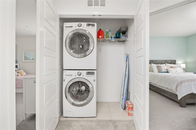 laundry area featuring stacked washer / dryer, light tile patterned floors, visible vents, light carpet, and laundry area