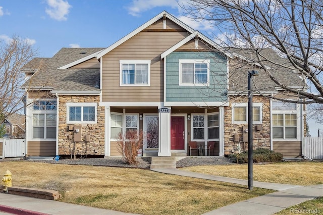 view of front of home featuring a front yard, fence, stone siding, and a shingled roof