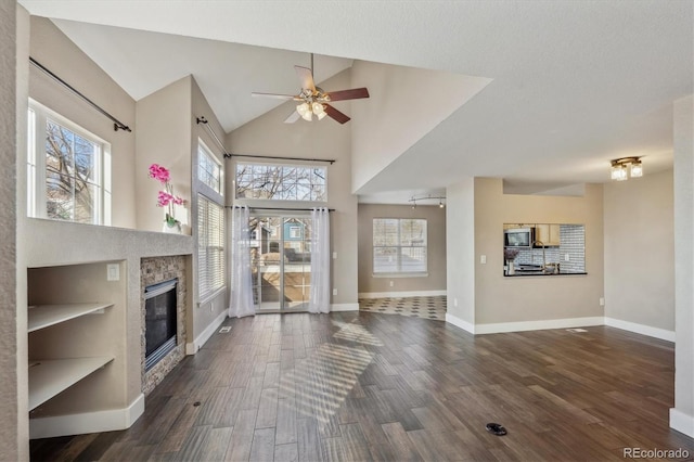 unfurnished living room featuring a glass covered fireplace, dark wood-type flooring, baseboards, and high vaulted ceiling