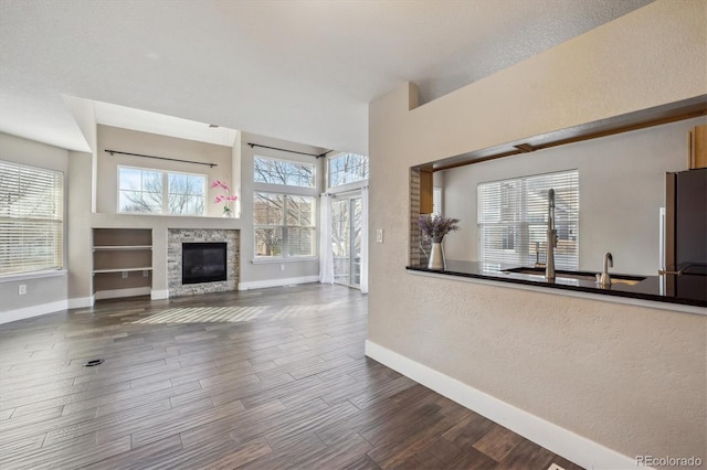 unfurnished living room with baseboards, a stone fireplace, and wood finished floors