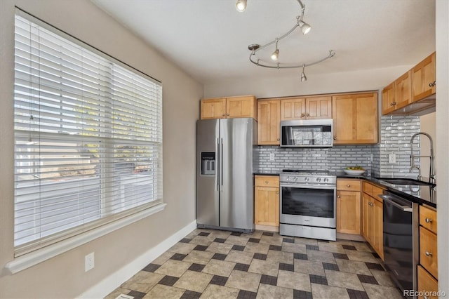 kitchen with a sink, backsplash, dark countertops, appliances with stainless steel finishes, and baseboards