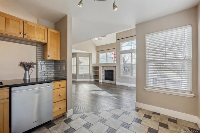 kitchen with a glass covered fireplace, baseboards, stainless steel dishwasher, dark countertops, and backsplash