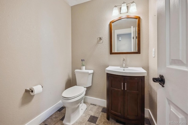 half bathroom with vanity, toilet, and baseboards