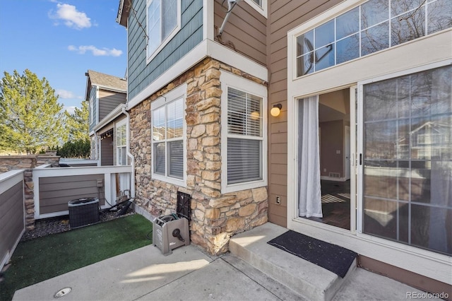 doorway to property featuring stone siding, central air condition unit, and a jacuzzi