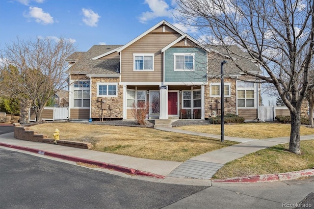 craftsman inspired home with stone siding, roof with shingles, a front lawn, and fence