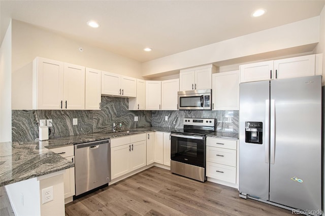 kitchen with kitchen peninsula, white cabinets, appliances with stainless steel finishes, dark stone counters, and dark hardwood / wood-style floors