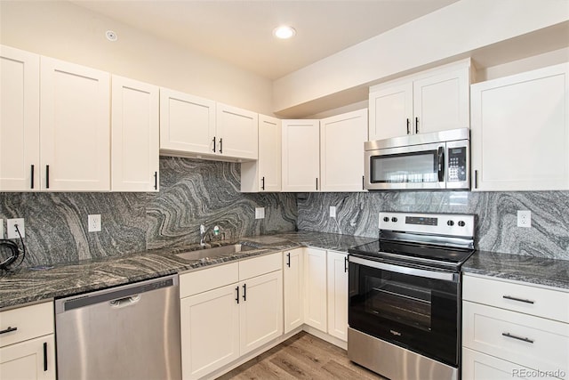 kitchen featuring white cabinets, tasteful backsplash, appliances with stainless steel finishes, dark stone countertops, and light hardwood / wood-style floors