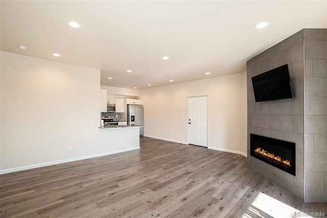 unfurnished living room with a tiled fireplace and light wood-type flooring