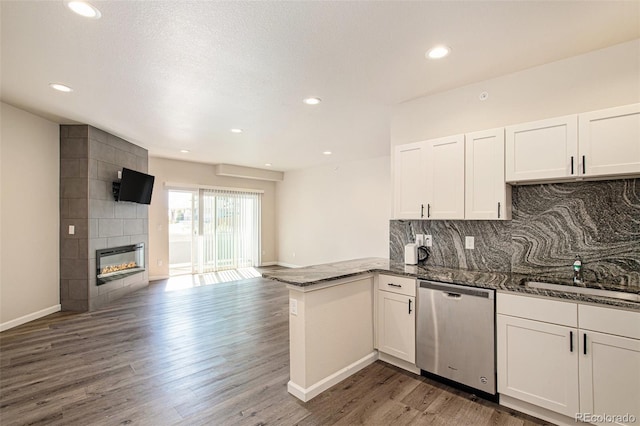 kitchen featuring dishwasher, dark hardwood / wood-style flooring, kitchen peninsula, white cabinetry, and a tiled fireplace