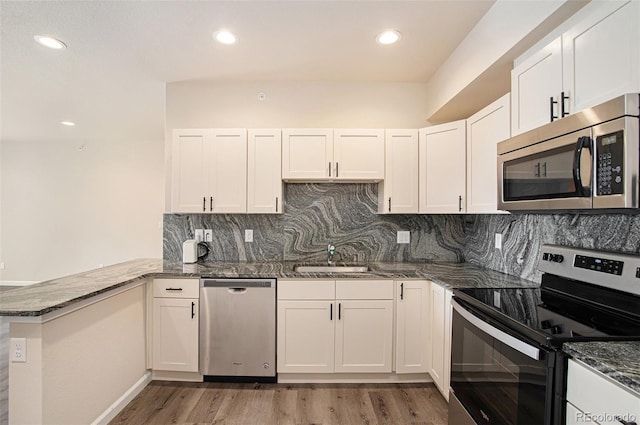 kitchen featuring wood-type flooring, backsplash, kitchen peninsula, white cabinetry, and stainless steel appliances