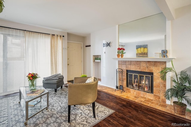 living area featuring a tile fireplace, baseboards, and wood finished floors