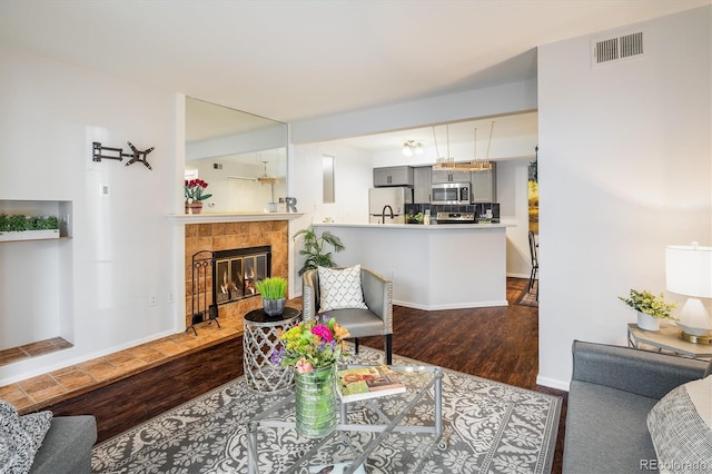 living room featuring a tiled fireplace, wood finished floors, visible vents, and baseboards