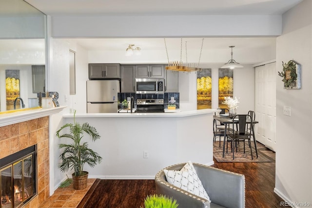 kitchen featuring stainless steel appliances, a fireplace, gray cabinetry, and dark wood-style floors