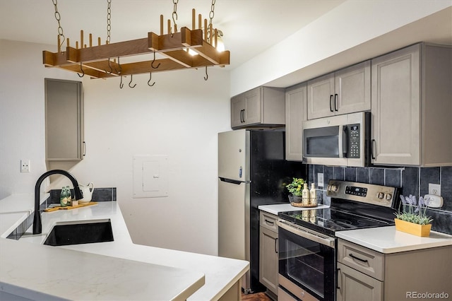 kitchen featuring appliances with stainless steel finishes, light countertops, a sink, and gray cabinetry