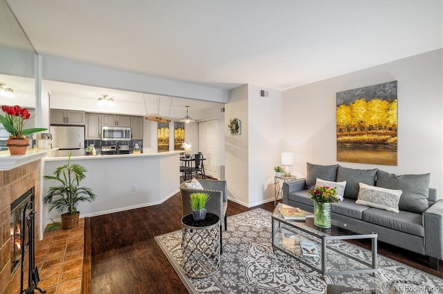 living area with visible vents, baseboards, dark wood-style flooring, and a tile fireplace