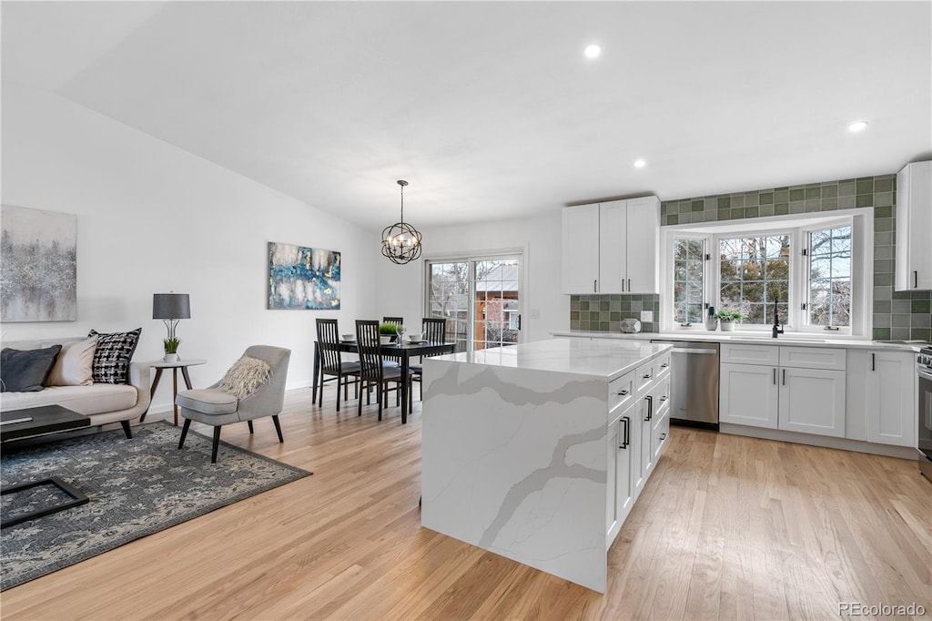 kitchen featuring light stone counters, decorative light fixtures, dishwasher, and white cabinets