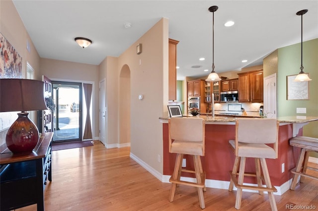 kitchen with light stone counters, a kitchen breakfast bar, light hardwood / wood-style floors, kitchen peninsula, and hanging light fixtures