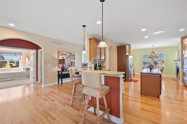 kitchen with hanging light fixtures, light hardwood / wood-style floors, stainless steel fridge, and kitchen peninsula