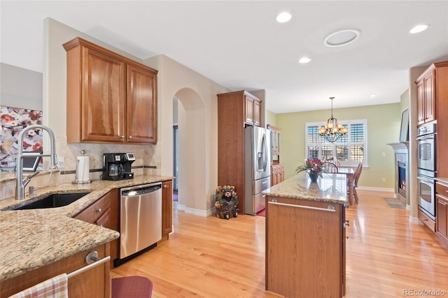 kitchen with sink, stainless steel appliances, light stone counters, and pendant lighting