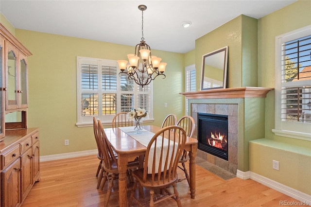 dining room with an inviting chandelier, light hardwood / wood-style floors, and a tiled fireplace