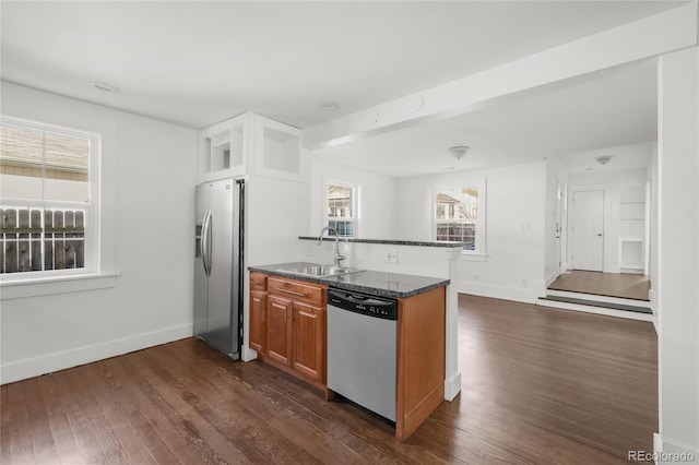 kitchen with kitchen peninsula, dark hardwood / wood-style flooring, sink, dark stone countertops, and stainless steel appliances