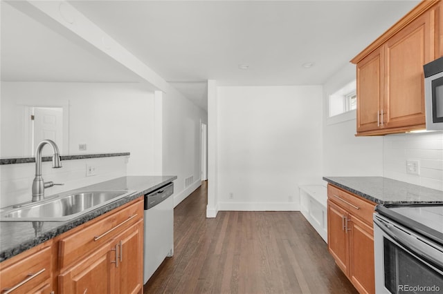 kitchen featuring appliances with stainless steel finishes, dark hardwood / wood-style flooring, dark stone countertops, sink, and backsplash